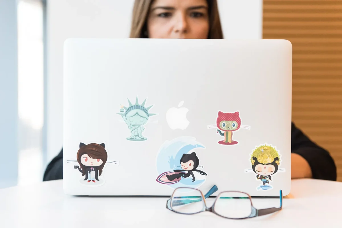 Person working on a laptop covered in stickers. Via Unsplash