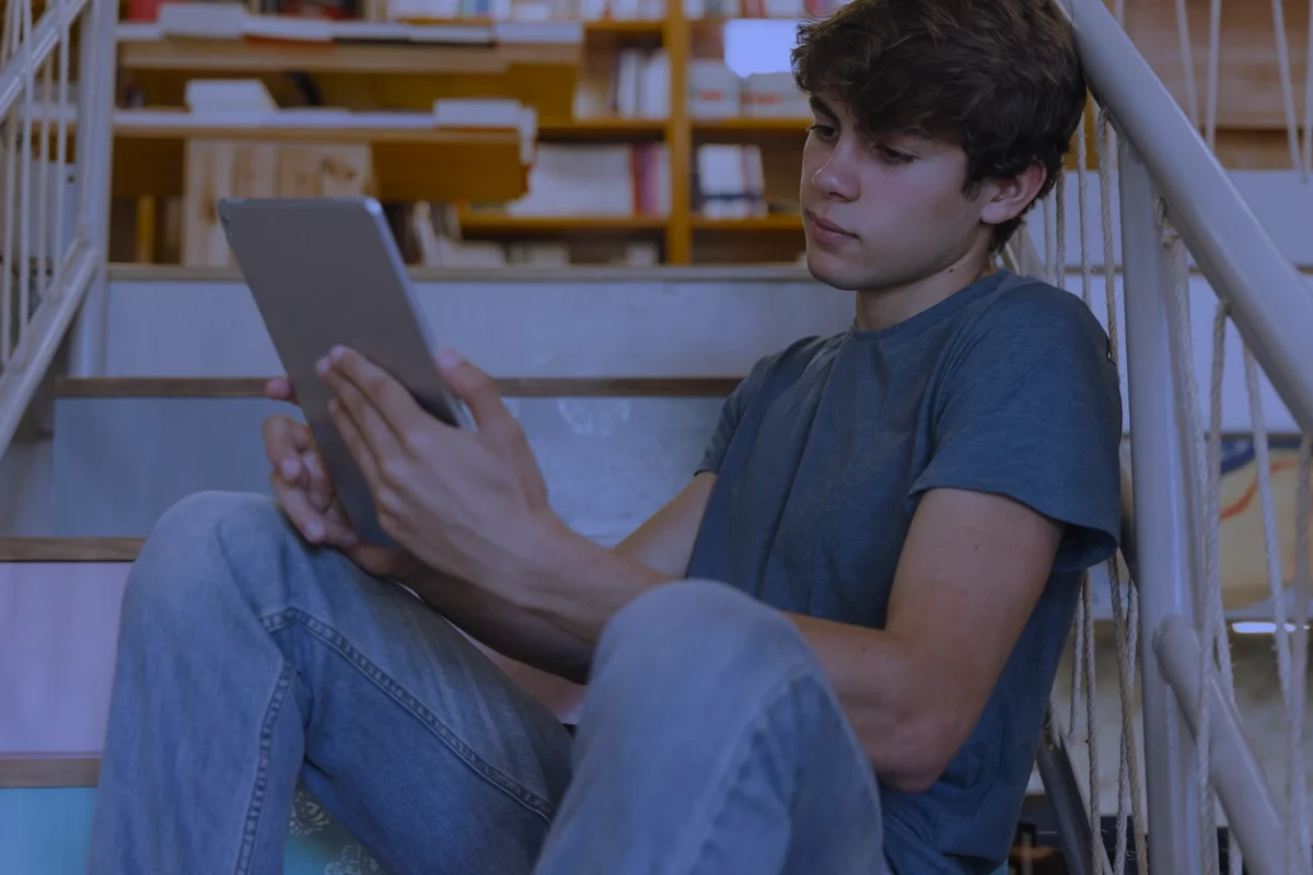 Boy reading his digital device in a library via Freepix